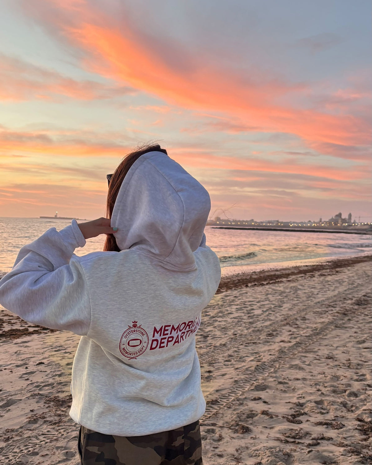 Espalda de la Hoodie MEMORIES gris con Memories Department, puesta en la playa de Cádiz al atardecer
